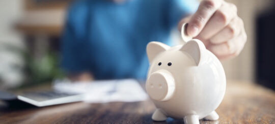 person putting money in a piggy bank to reflect the concept of saving in a pension