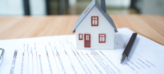 a rental agreement on a desk with a small house model on top of it